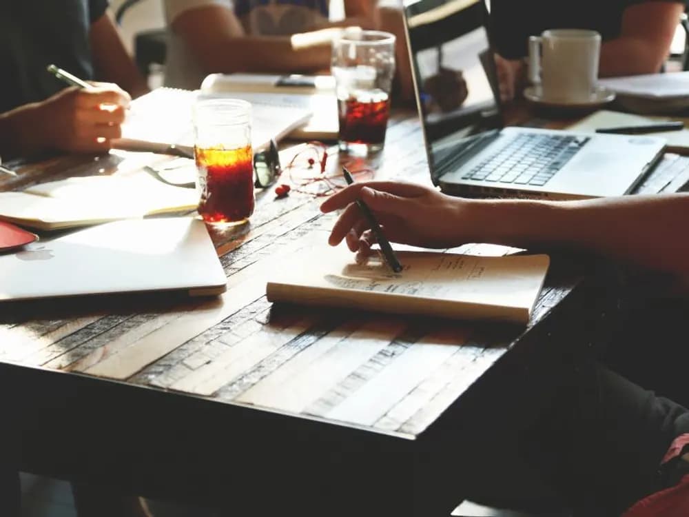 Une équipe travaille autour d'une table, ordinateurs portables et carnets ouverts.